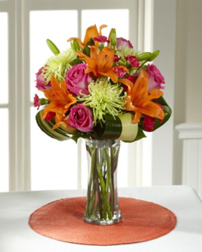 <p>Hot pink bi-colored roses, orange Asiatic Lilies, green Fuji Chrysanthemums, hot pink mini carnations, tropical leaves, and lush greens are brought together to impress, presented in a clear glass vase. Bright, beautiful, and ready to get the party started, this bouquet creates a unique surprise to absolutely delight your recipient with each sunlit bloom.</p>